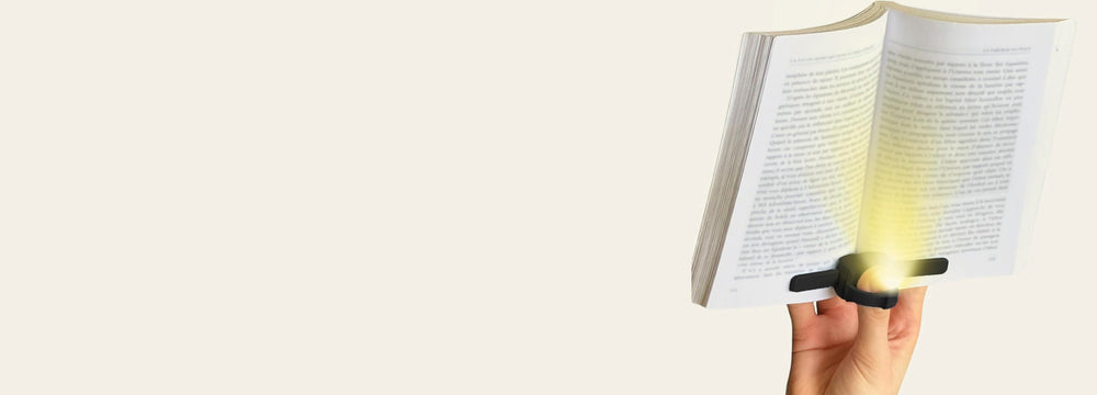 Hand holding a paperback open one-handed with the black Lizia book light lighting the page
