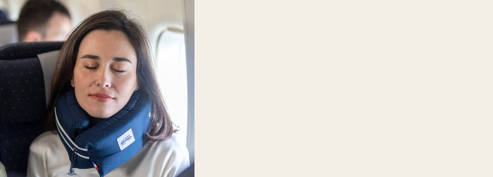 Woman asleep in a plane seat wearing the navy Le Petit Dormeur travel pillow around her neck